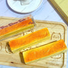 A rectangular orange butter stick squishy toy is displayed on a wooden cutting board.
