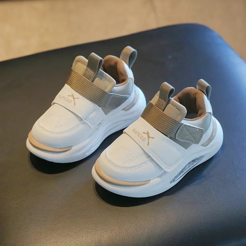 A pair of light gray and white kids' everyday sneakers with tan lining resting on a dark surface.