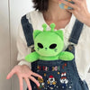 A hand holds a bright green Kawaii Alien Cat plush toy against a white shirt and denim overalls.