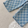 A close-up of blue plaid corduroy pants folded on a light beige fabric with white lace visible below.