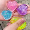 Hand holding four heart-shaped squishy toys in pink, purple, blue, and yellow colors