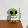 Handmade crochet pocket hug doll shaped like a green alien with black eyes and an inspirational slogan tag