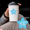 A hand holds a white disposable coffee cup with a light blue star design on it.