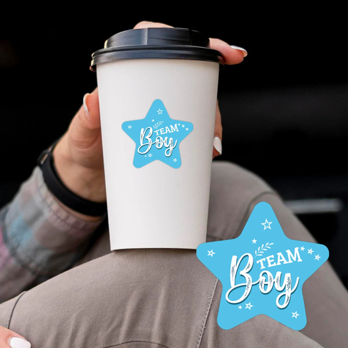 A hand holds a white disposable coffee cup with a light blue star design on it.