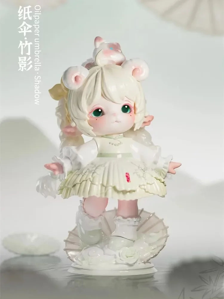 A white collectible figurine of a girl with pink hair and large ears, wearing a white dress, displayed against a light backgr