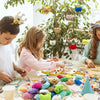 A child is assembling an assorted mini animal plush toy set with keychain loops on a table surrounded by greenery.