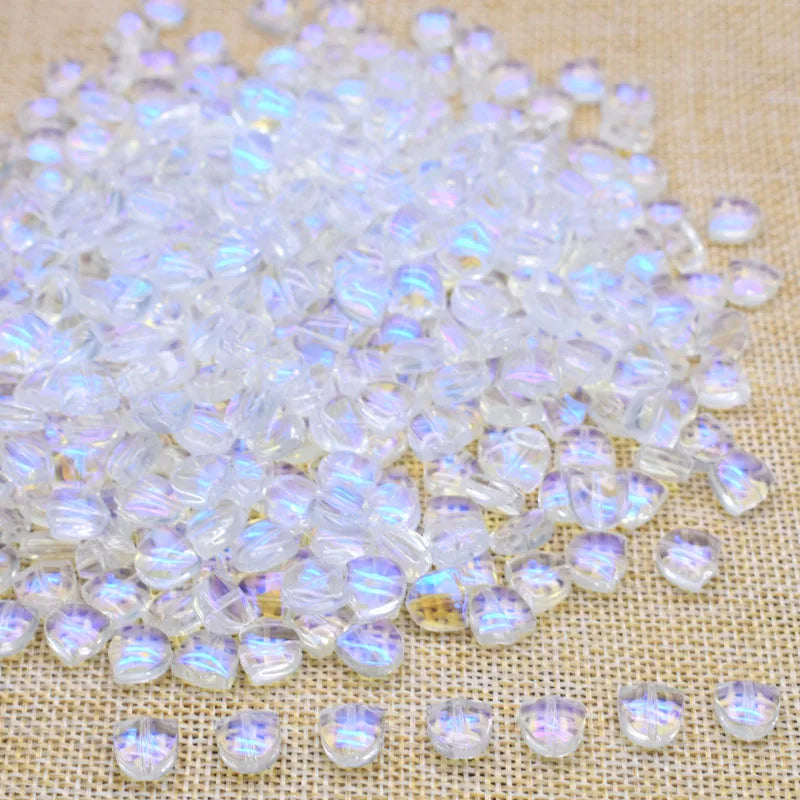 A pile of clear, iridescent tulip flower glass beads scattered on a light-colored fabric.