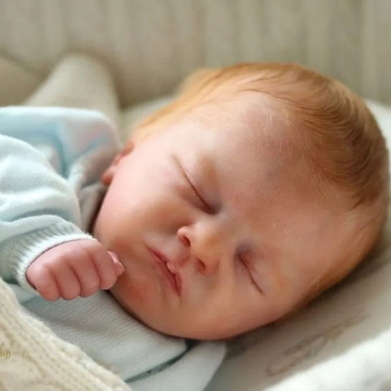 A newborn baby with light skin and reddish hair is sleeping peacefully, resting on a soft white cloth.