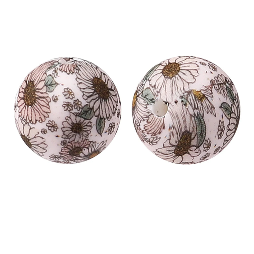 Two round silicone beads with a floral pattern featuring daisies and green leaves on a white background