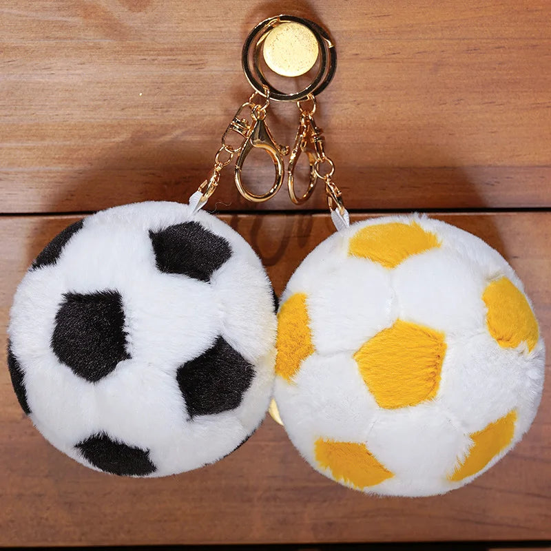 A white and black plush soccer ball toy with a gold chain attached, resting on a wooden surface.