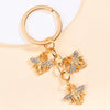 Gold-toned enamel flower keychain featuring a bee design on a white background.