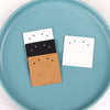 A stack of square kraft jewelry display cards with black and white designs rests on a light blue plate.