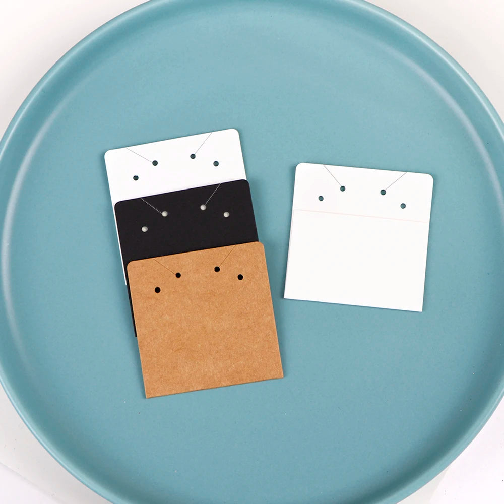 A stack of square kraft jewelry display cards with black and white designs rests on a light blue plate.