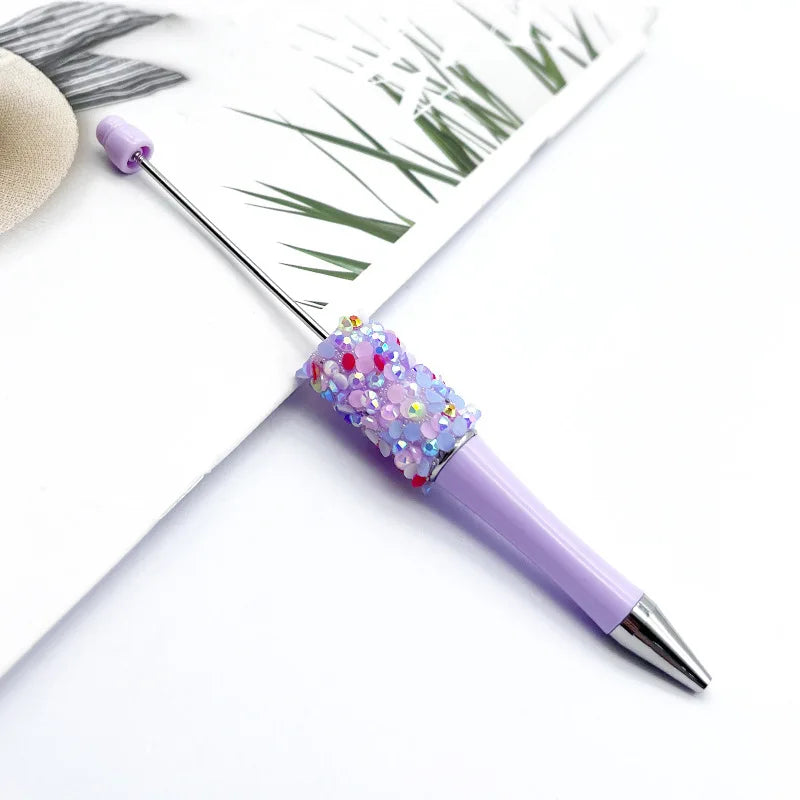 A purple ballpoint pen with a sequin bead ball is shown next to a piece of paper featuring a green leaf design.