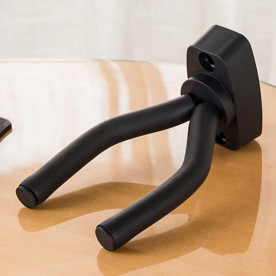 A black wall-mounted guitar holder with a curved cradle resting on a wooden surface.