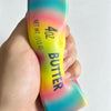 A hand holds a yellow squishy fidget toy with rainbow colored gradients and the text 40Z BUTTER NET WT 113G on it.