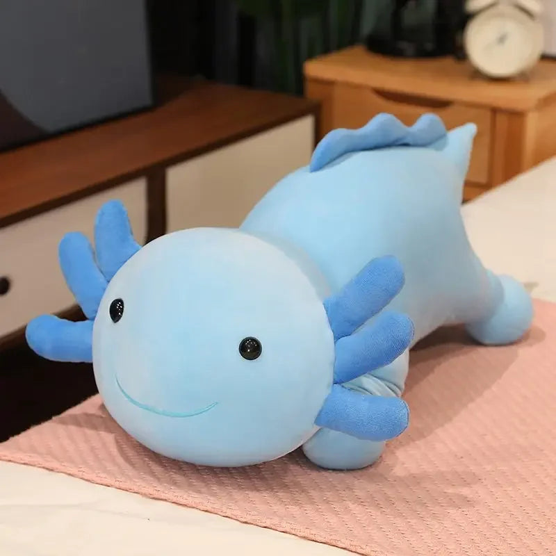 A light blue axolotl plush pillow with blue gills resting on a pink surface.