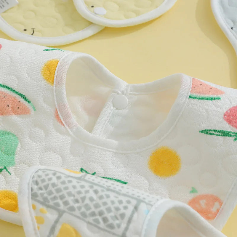 A close-up view of a white baby bib with colorful fruit patterns and a gray patterned bib in a set.