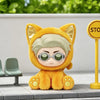 An orange cat-shaped collectible figure with white hair and round glasses sits on a gray surface.