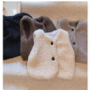 A collection of three plush fleece vests in shades of black, brown, and cream resting on a light-colored surface.