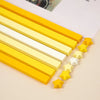 A collection of yellow and white origami star strips laid out diagonally on a light surface.