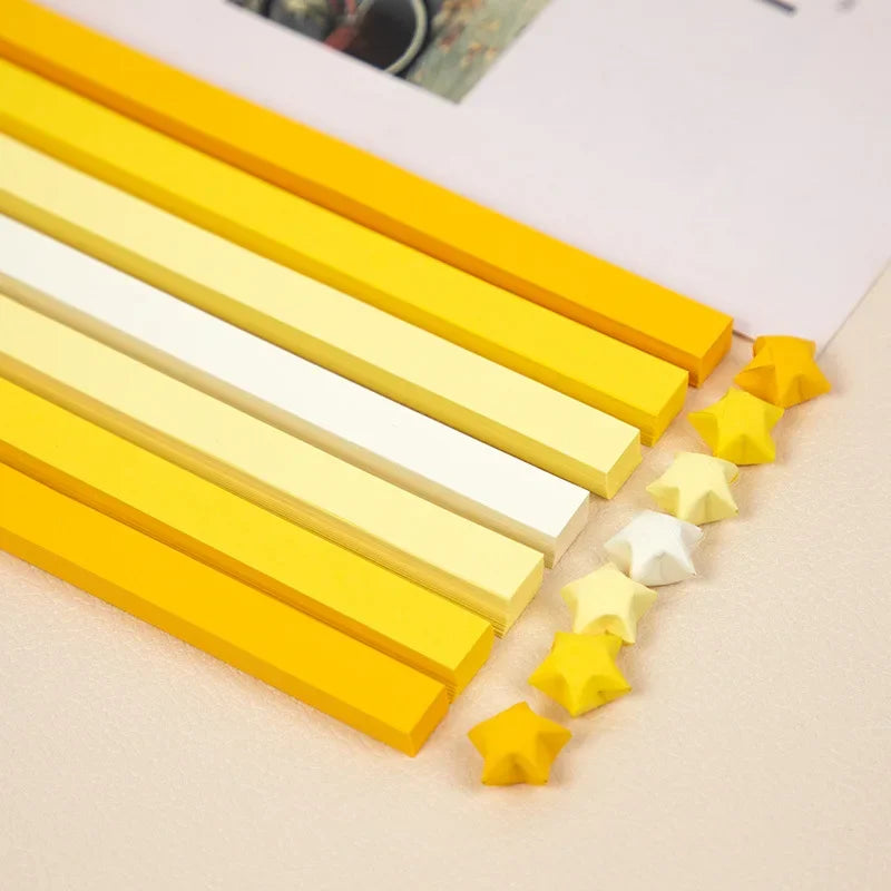 A collection of yellow and white origami star strips laid out diagonally on a light surface.