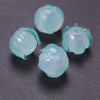 Several translucent mint green glass charm pendants shaped like lily of the valley blooms are displayed on a dark surface.