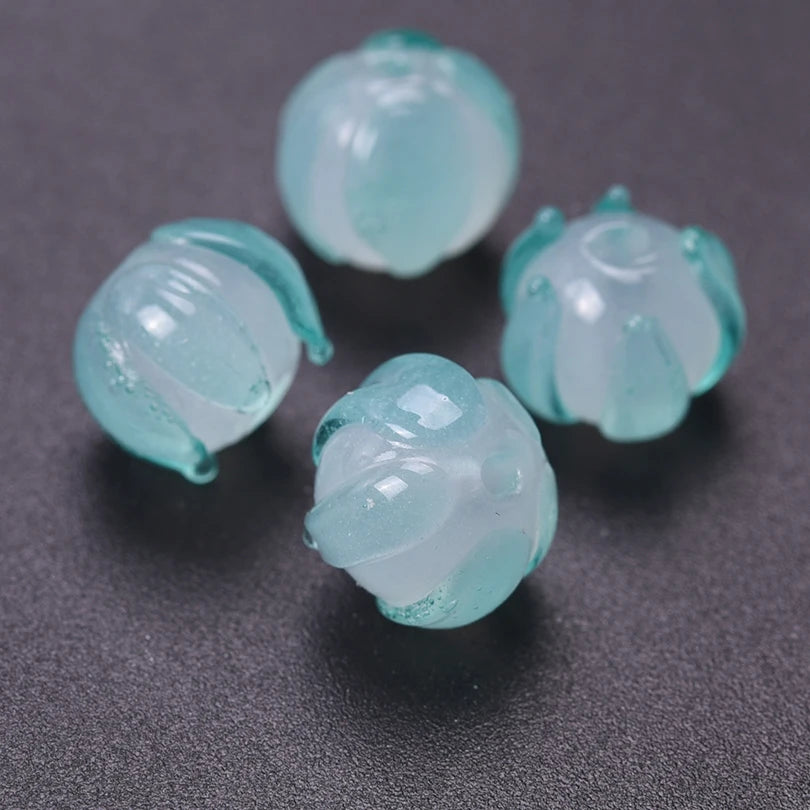 Several translucent mint green glass charm pendants shaped like lily of the valley blooms are displayed on a dark surface.