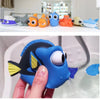 A hand holds a blue rubber fish bath toy that is squirting water in a sink.