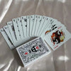 A deck of black and white poker cards is fanned out on a light fabric background.