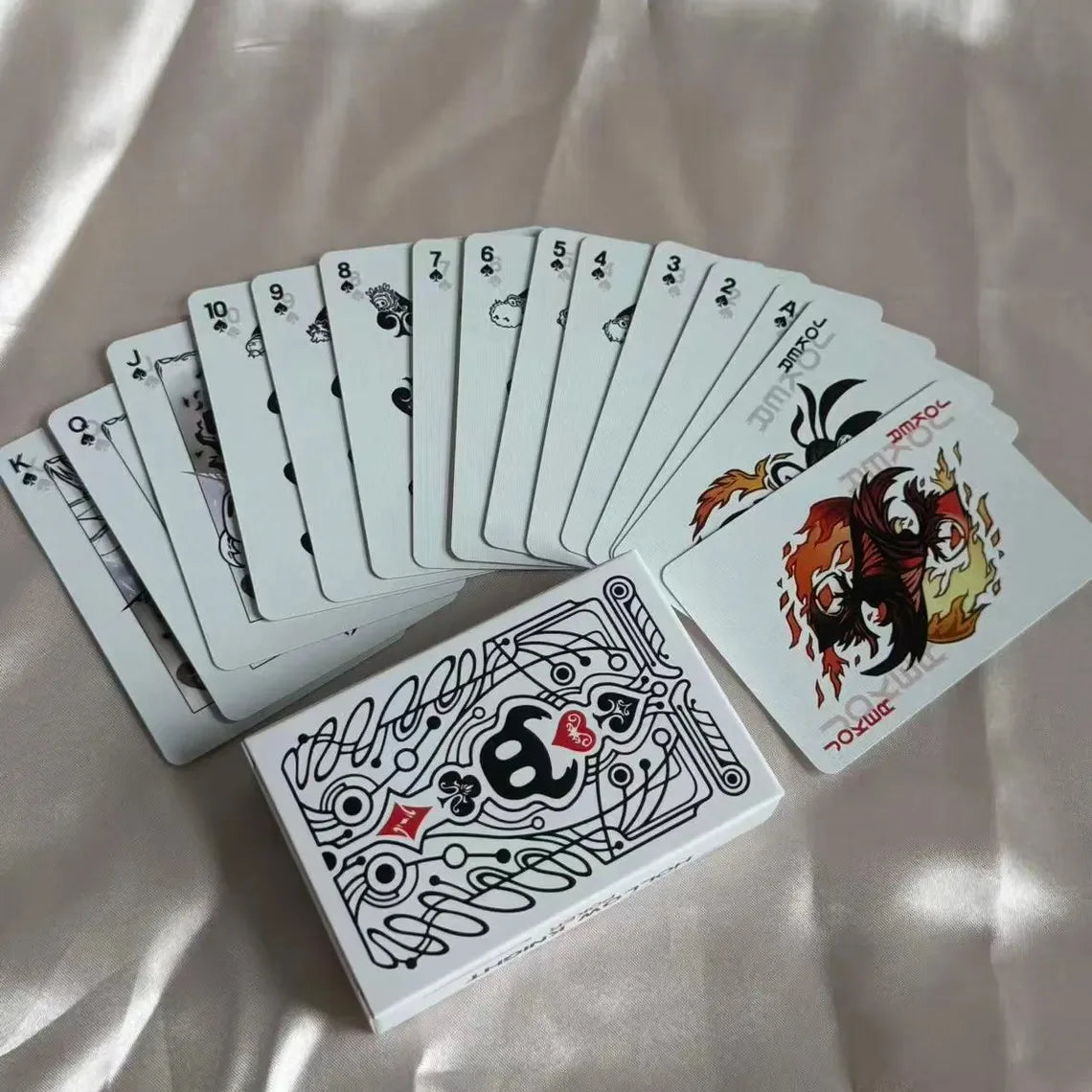 A deck of black and white poker cards is fanned out on a light fabric background.