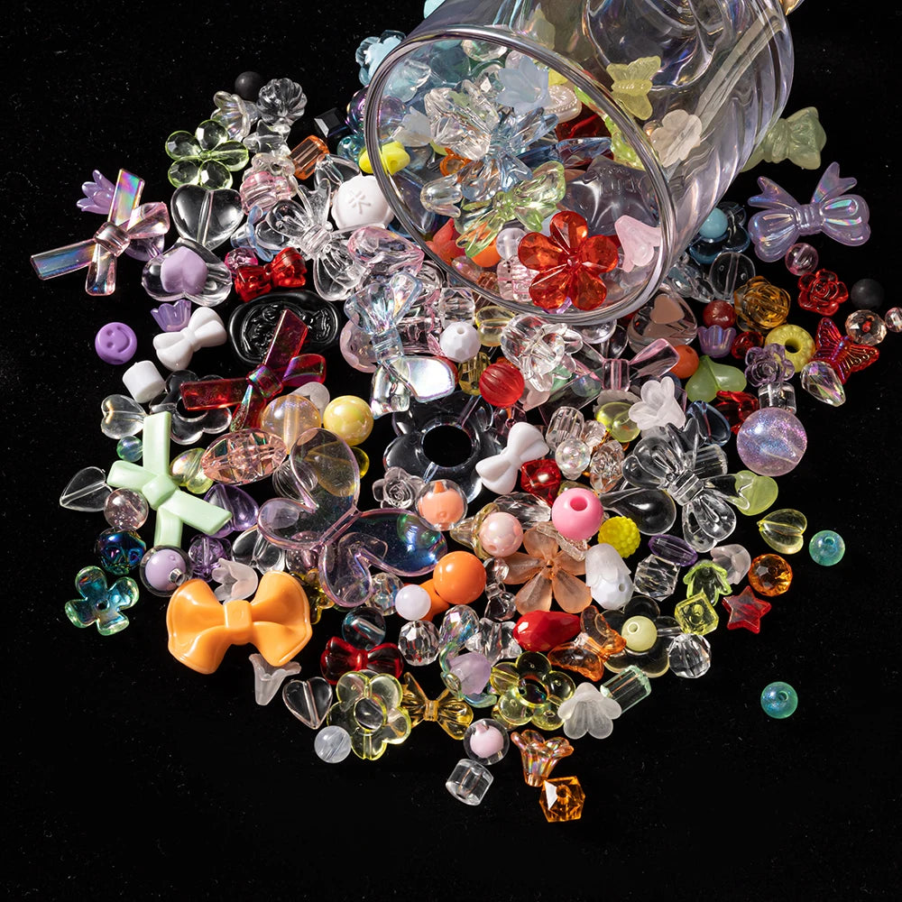 A collection of mixed clear and colored acrylic bow and flower beads scattered on a dark surface.