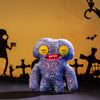 A purple monster plush doll with large teeth and yellow eyes is displayed against a dark background.
