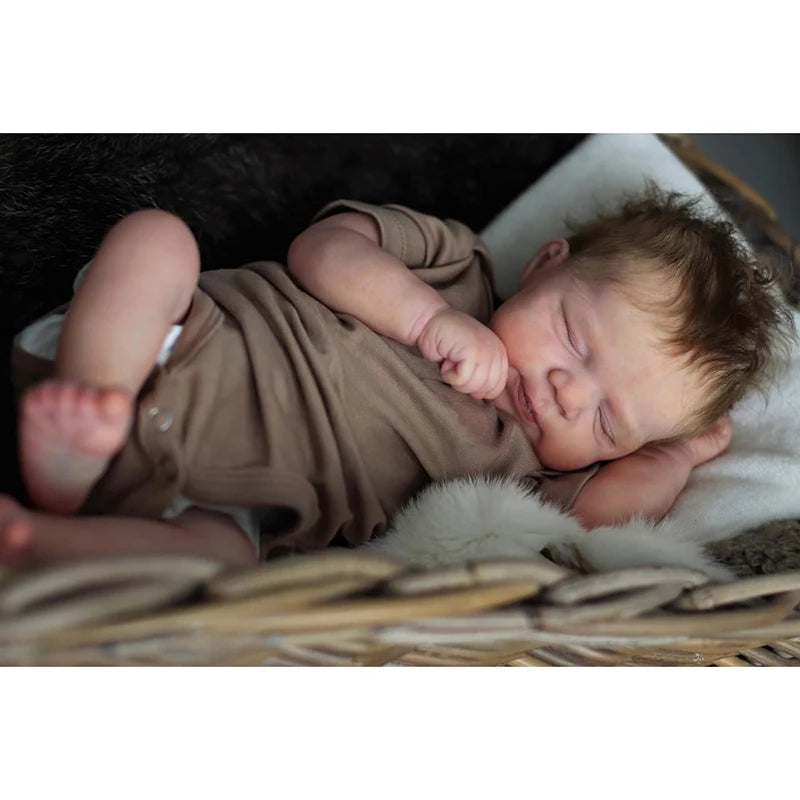 A newborn baby doll with rooted hair sleeping peacefully on a soft, white blanket.