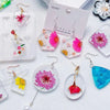 A collection of clear epoxy resin earrings and pendants featuring floral designs in pink, yellow, and blue colors.