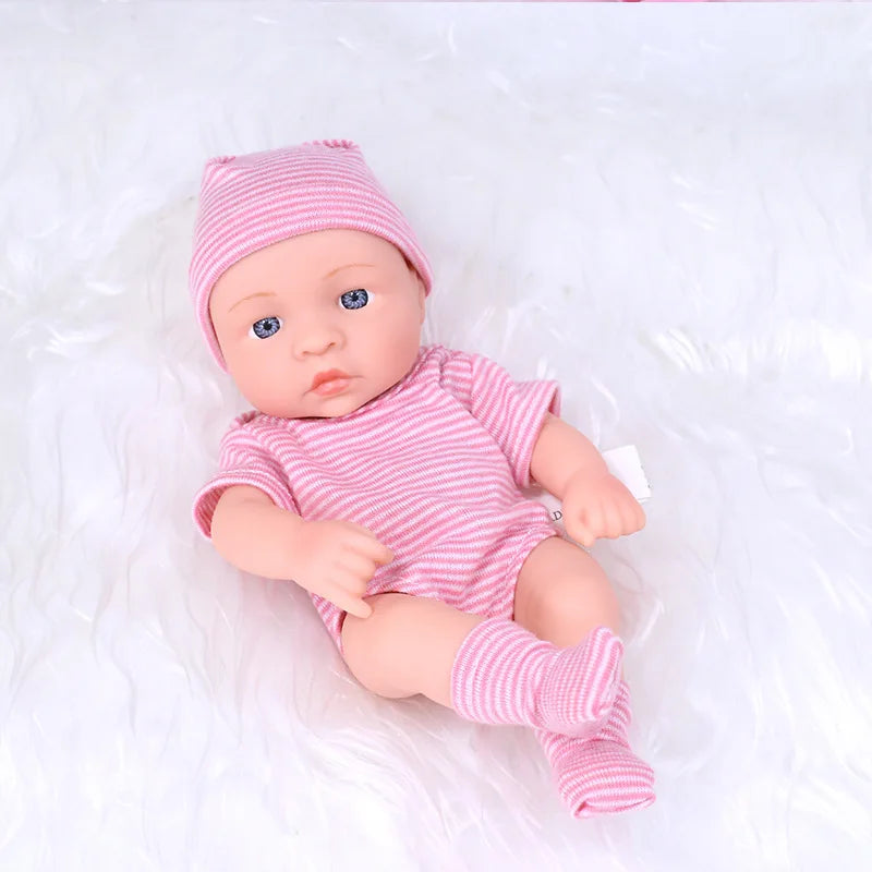 A realistic soft vinyl reborn baby doll wearing a pink striped outfit and matching hat, lying on white fluffy material.