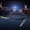 A coiled black instrument cable with a male connector is displayed in front of a band performing on stage.