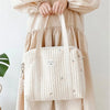 A light beige quilted diaper bag with embroidery carried by a person wearing a flowing cream-colored maternity dress.