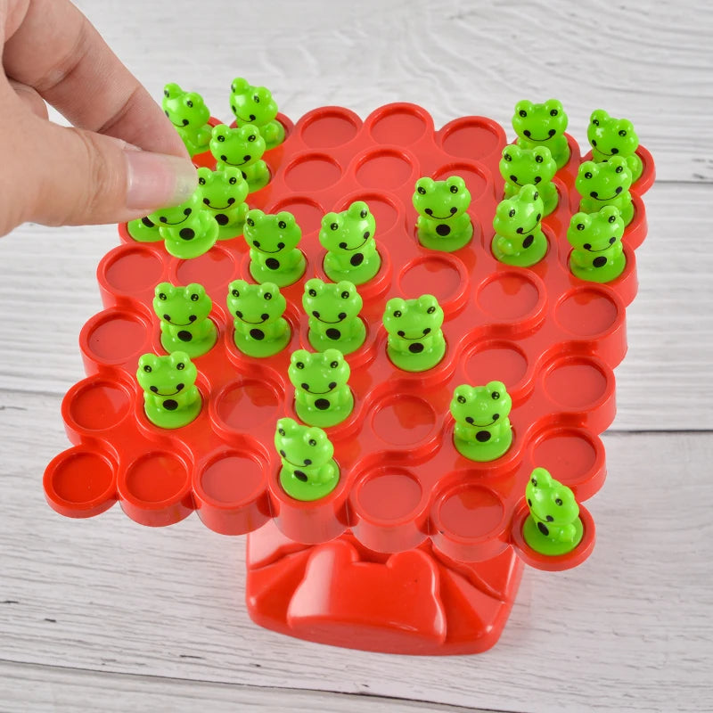 A hand is placing small green frog-shaped pieces into a red plastic grid for a balance game.