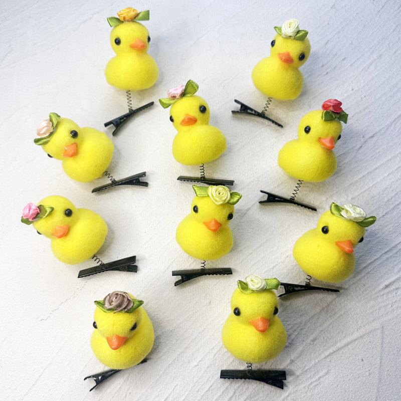 A collection of yellow duck plush hair clips with small green accents arranged on a white background.