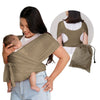 A woman wearing a olive green X-shaped baby sling carrier while holding a baby.