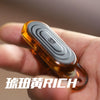 A hand holds an amber-colored EDC push slider fidget toy with a silver ring.