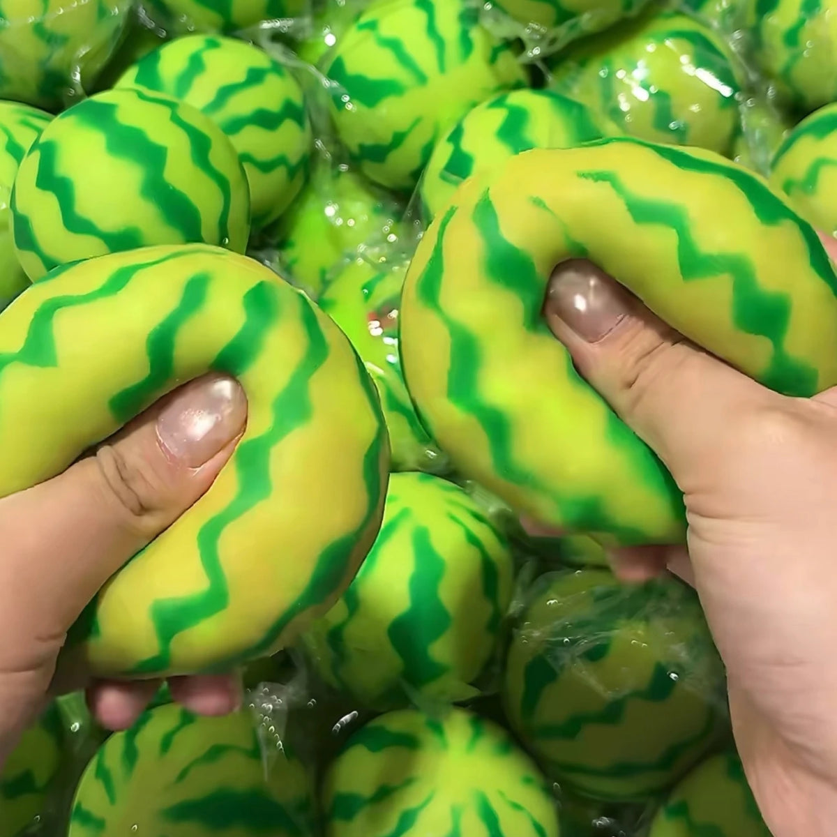 A hand holds a bright green watermelon squishy stress ball with a striped texture.