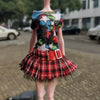 A doll wearing a colorful top and a red plaid skirt.