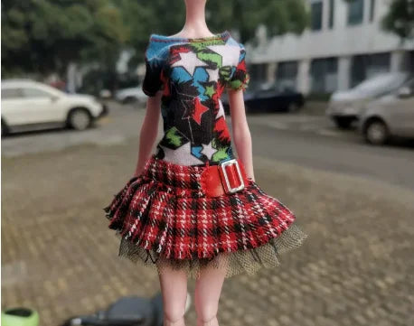 A doll wearing a colorful top and a red plaid skirt.