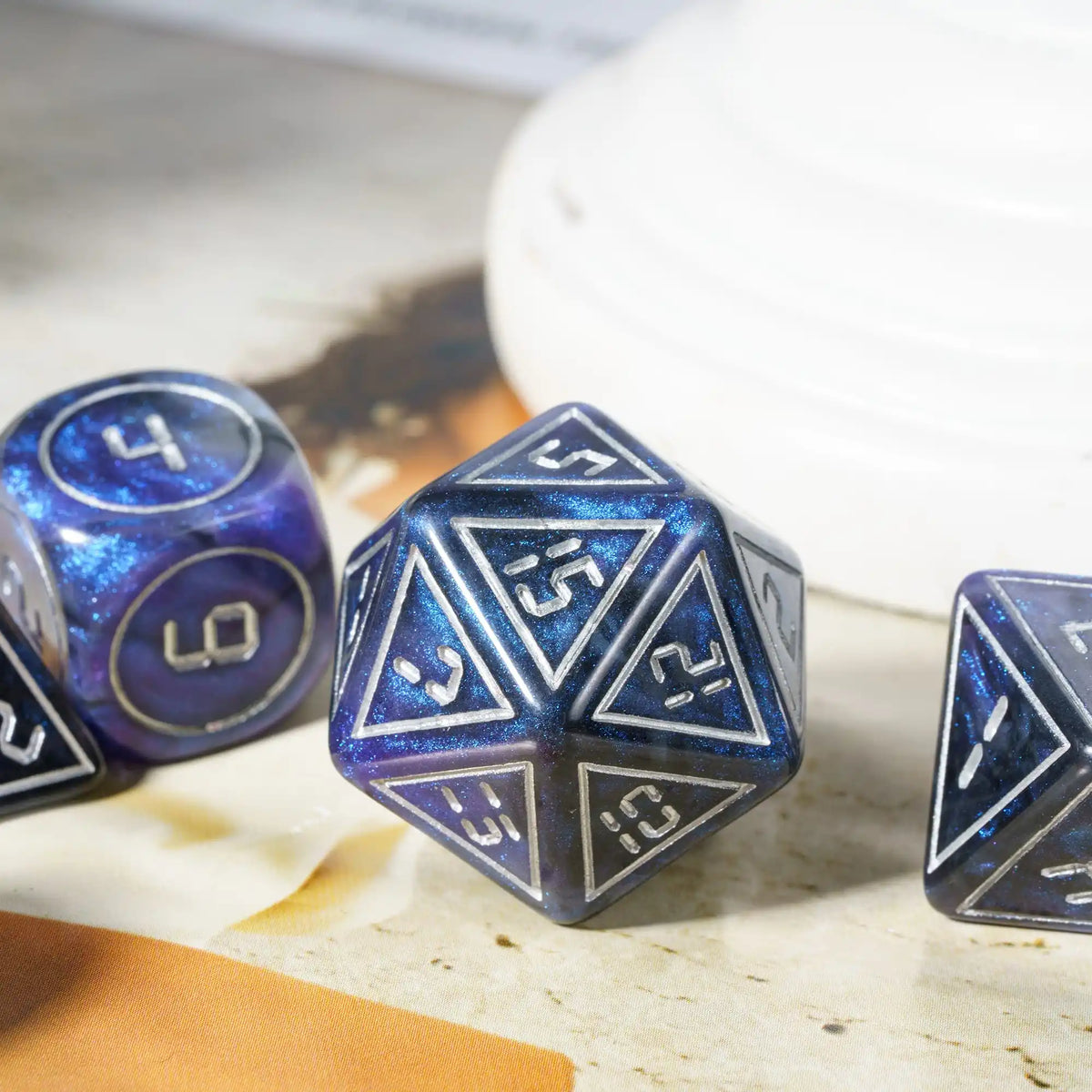 A close-up of a set of seven blue and purple resin polyhedral dice resting on a light surface.
