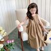A young girl wearing a beige sleeveless cotton sundress sits in a light-colored chair.