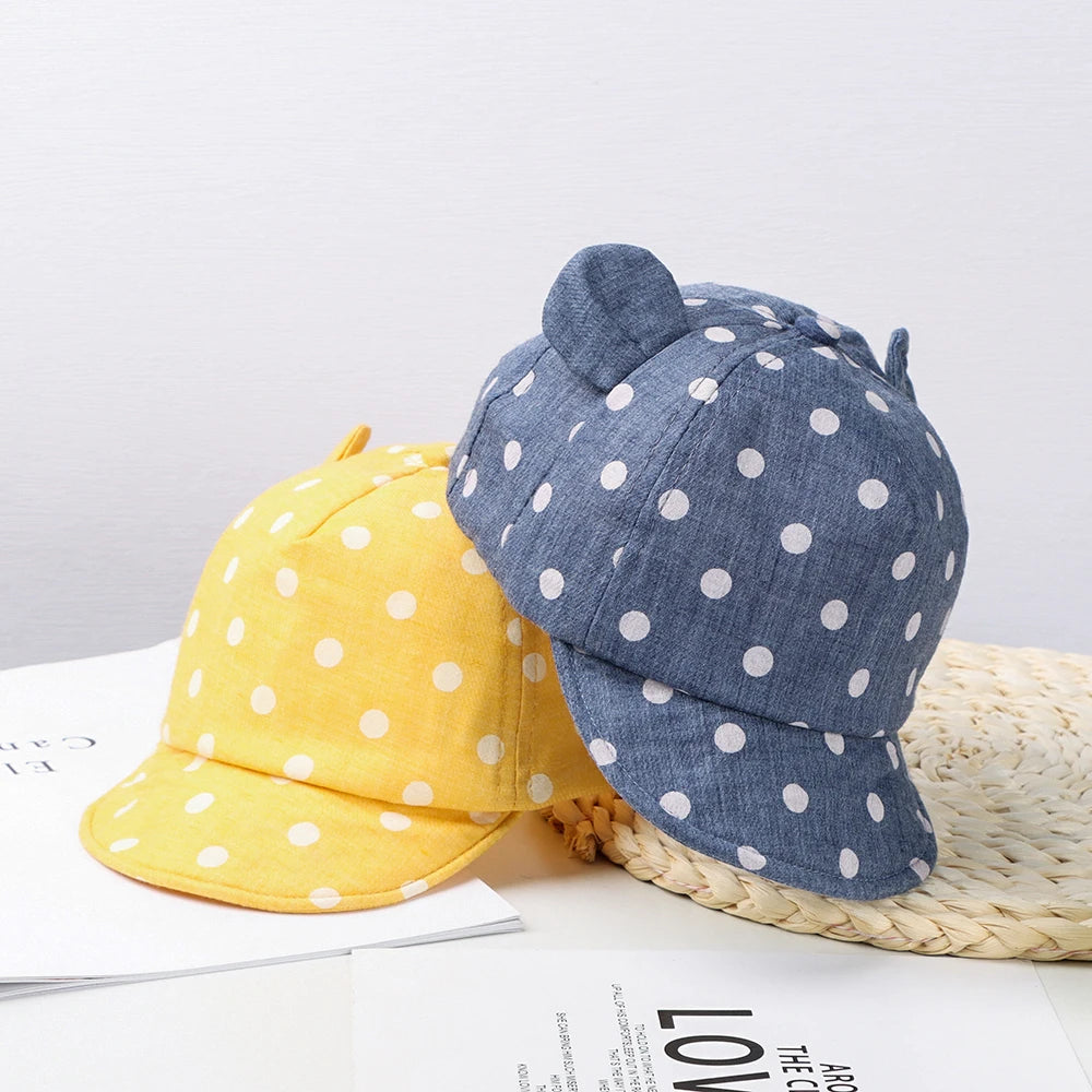 A blue denim baseball cap with white polka dots and a yellow cotton baseball cap with white polka dots resting on a woven mat