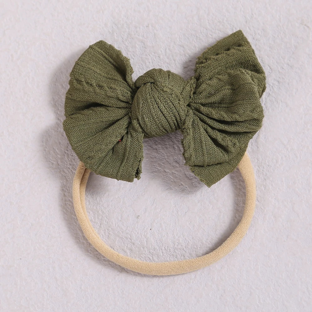 A soft olive green fabric bow headband with a light beige elastic band.