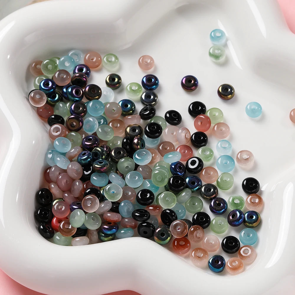 A collection of small, round imitation jade glass spacer beads in various shades of green, blue, and pink are displayed in a 